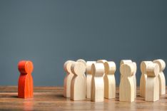 a group of wooden people pegs and 1 red peg on its own